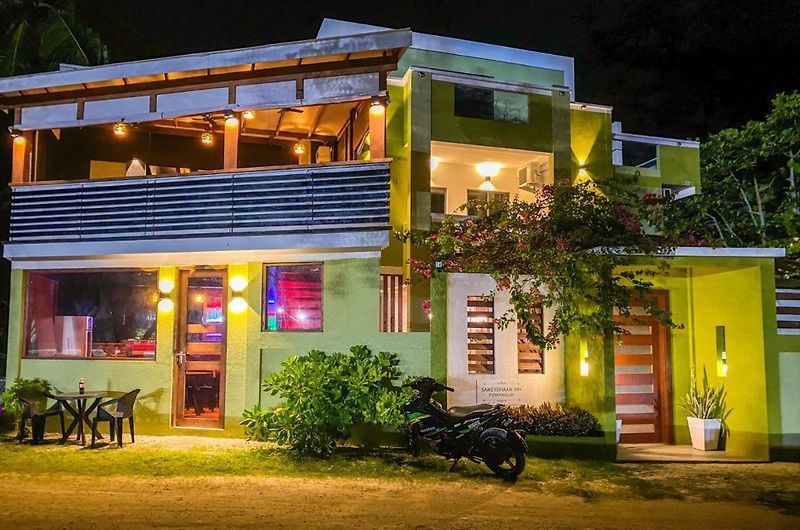 Cozy Roots Fuvahmulah lit up at night, with a table and chairs in the front garden