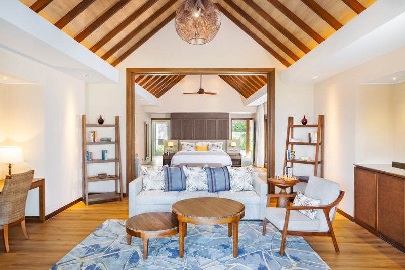 The living room of a Baros Suite with Private Pool at Baros Maldives, a sofa and round tables under a pitched timber ceiling.