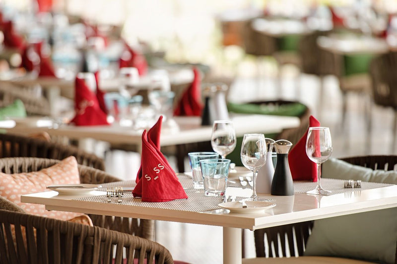 A restaurant table laid with glassware and red napkins at Hard Rock Hotel Maldives.