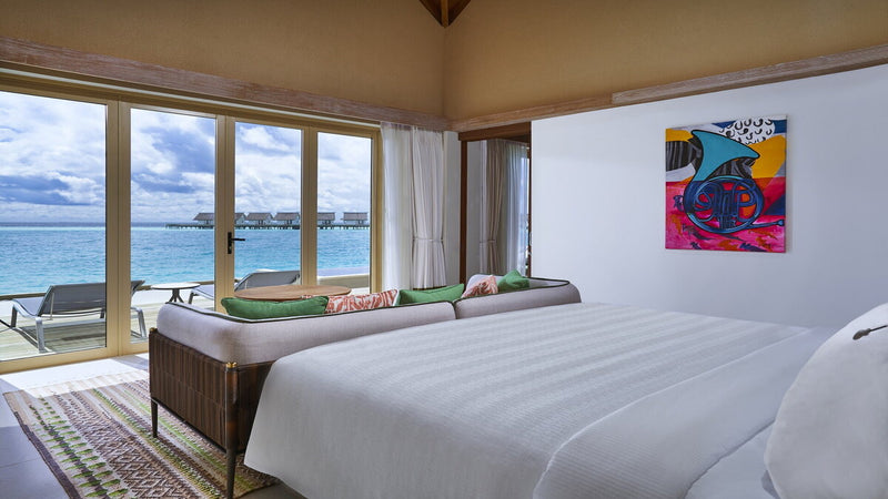 A bedroom in the Rock Royalty Overwater Pool Villa at Hard Rock Hotel Maldives, with a window seat above the lagoon.