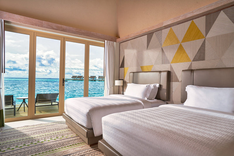 A twin bedroom at Hard Rock Hotel Maldives, opening onto a terrace above the water.