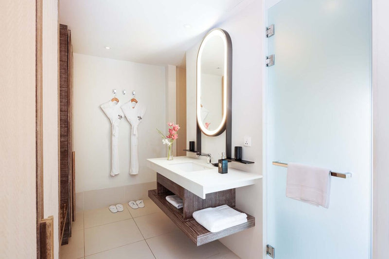 A villa bathroom at Hard Rock Hotel Maldives, twin robes beside an oval mirror and a stone vanity.