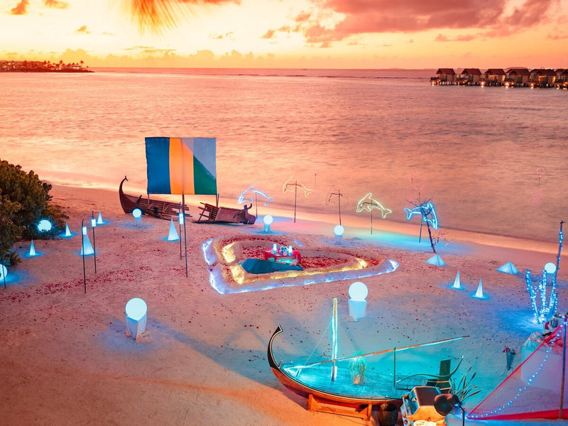 A private dinner laid on the beach at sunset at Hard Rock Hotel Maldives, lanterns around a sunken table.