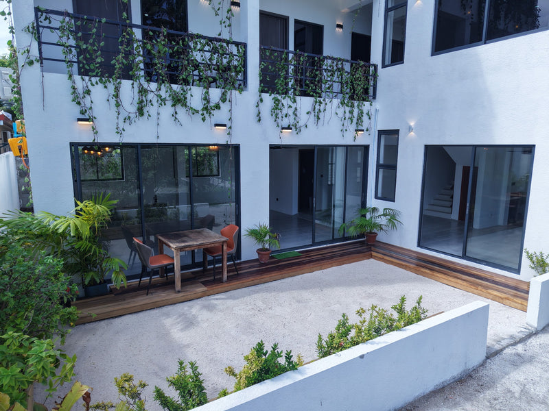 Sheltered courtyard at Cozy Art Dhangethi with a wooden deck, plants and glass doors to the rooms