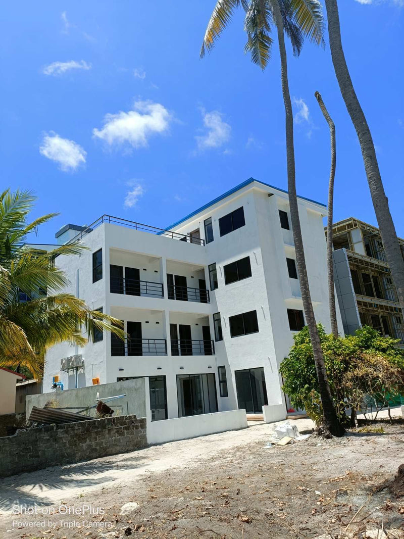 White exterior of Cozy Art Dhangethi with balconies on every floor under a blue sky