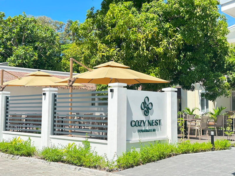Entrance to Cozy Nest Fuvahmulah with the hotel sign, a white gate and garden parasols
