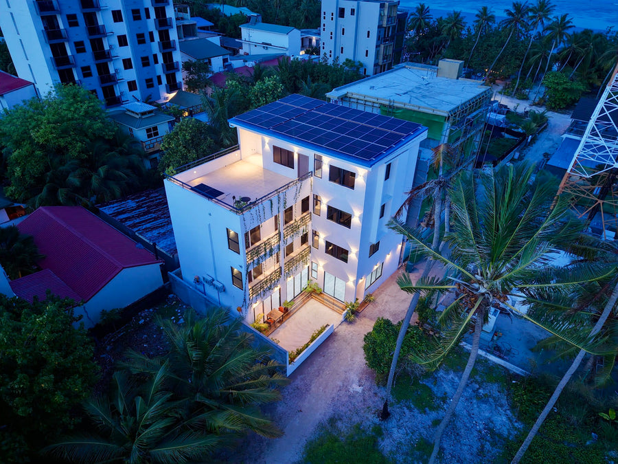 Cozy Art Dhangethi seen from the air at dusk, a white four-storey building lit among palm trees