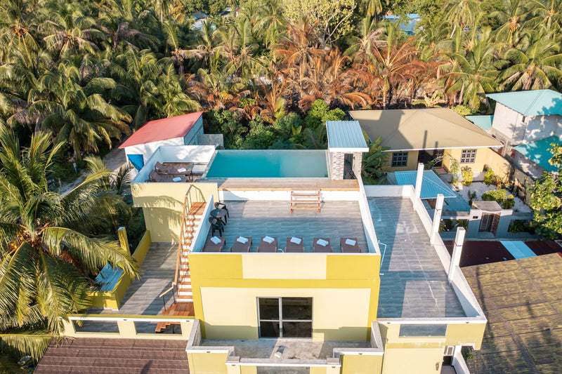 Cozy Roots Fuvahmulah from the air, its rooftop pool among palms and village houses