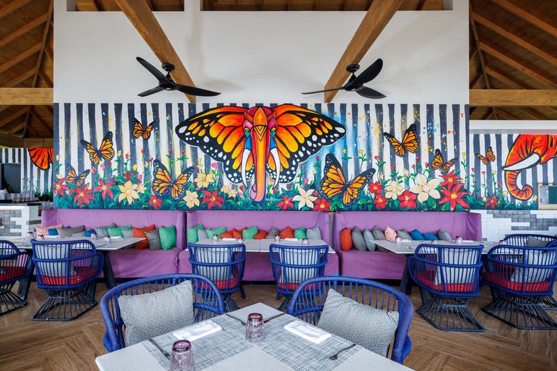 A restaurant at Hard Rock Hotel Maldives, a butterfly mural above the banquettes.