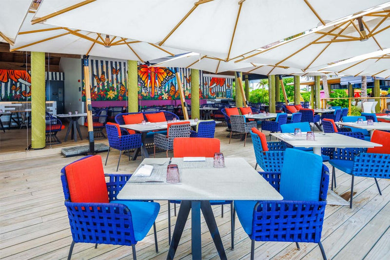 An open air restaurant at Hard Rock Hotel Maldives, blue and red chairs under canvas parasols.