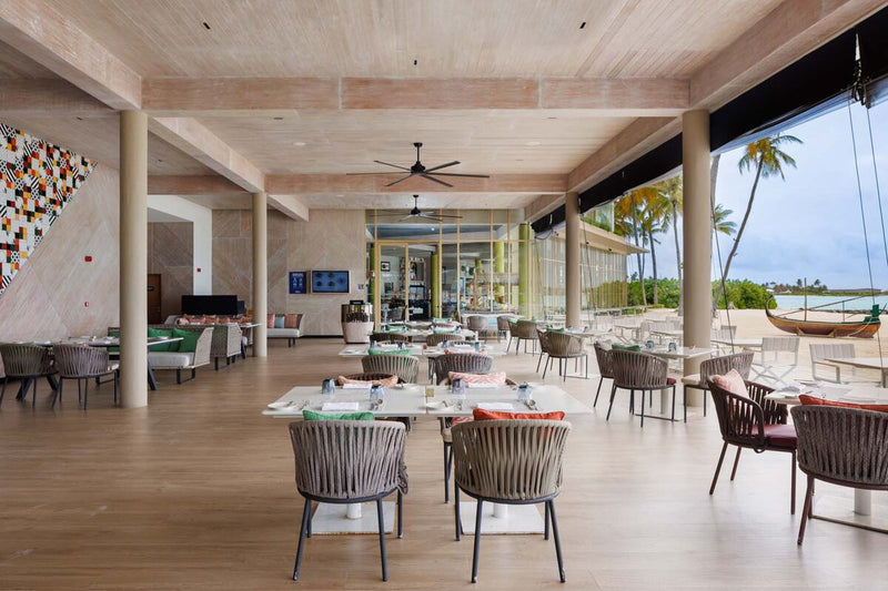 A restaurant interior at Hard Rock Hotel Maldives, rattan chairs and tables laid for service.