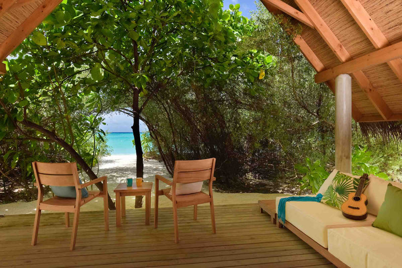 A beach villa at Fushifaru Maldives at sunset, armchairs and a guitar on the deck looking out to the beach
