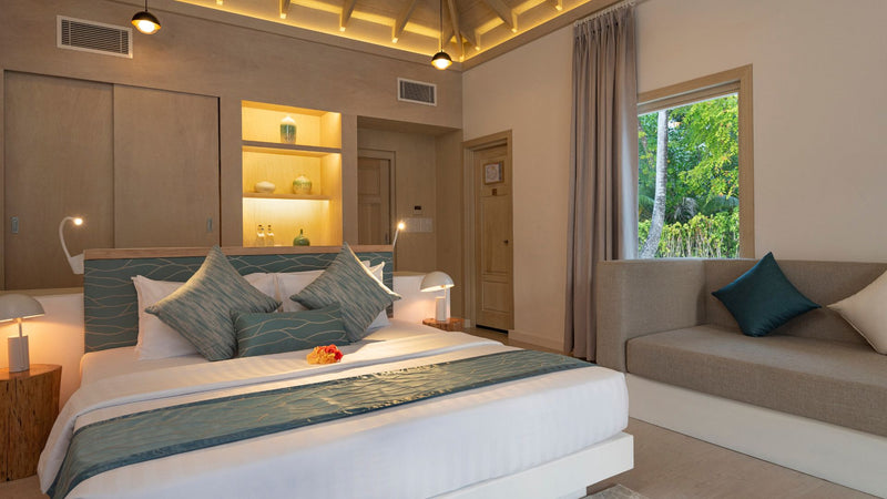 The bedroom of a Beach Villa at Bandos Maldives, with a sofa by the window.