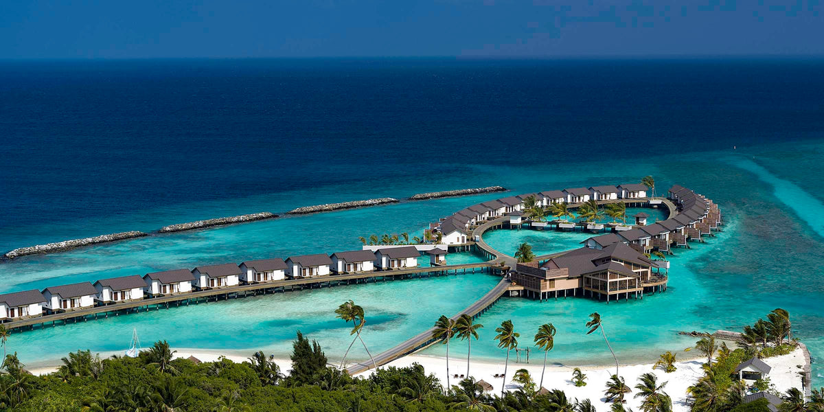 Atmosphere Kanifushi Maldives from the air, the long island edged by a jetty and a line of overwater villas