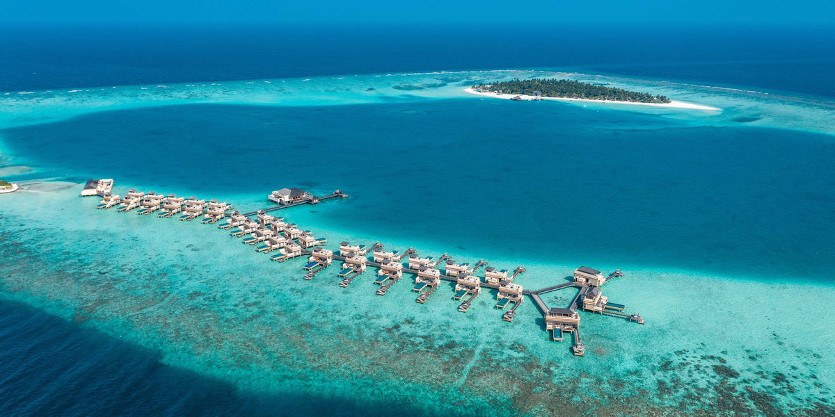 Angsana Velavaru from the air, the wooded island inside its reef with the overwater villas set well out in the lagoon