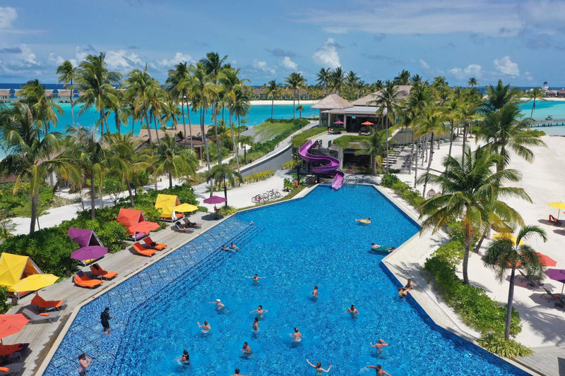 The main pool at Hard Rock Hotel Maldives, ringed with coloured loungers and palms.