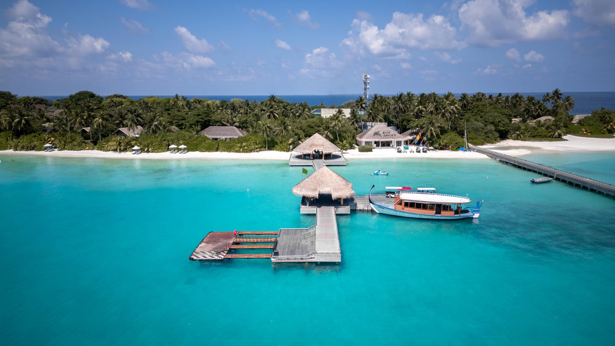 A resort arrival jetty reaching out over a turquoise lagoon, with a boat moored alongside.