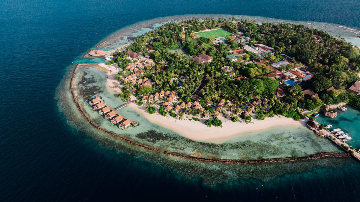An aerial view of Bandos Maldives, its beach, water villas and the reef around the island.