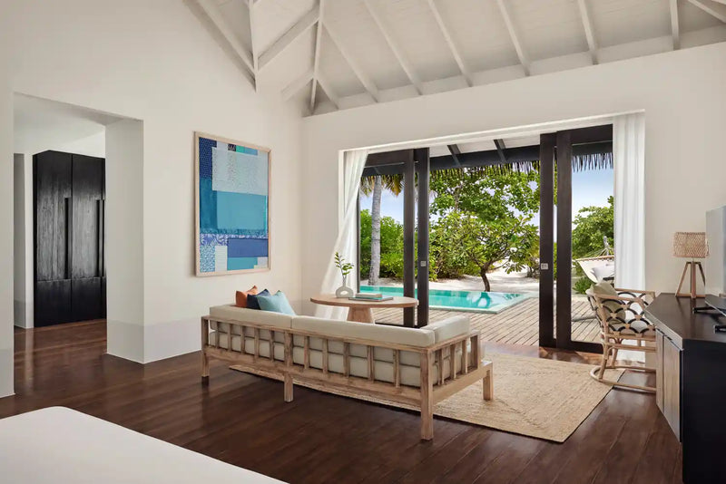 A beach villa interior at Noku Maldives, doors framing a turquoise plunge pool and greenery.