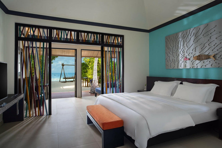 A Beachfront Villa bedroom at Dhawa Ihuru, orange bench at the bed and doors open to a beach swing.
