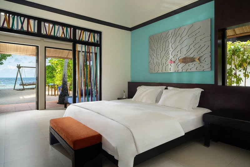 A villa bedroom at Dhawa Ihuru, turquoise wall relief above the bed and doors onto a garden swing.