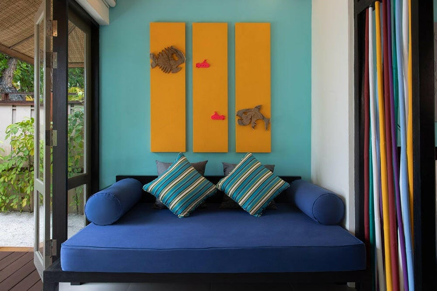 A blue daybed at Dhawa Ihuru, teal striped cushions under orange fish panels on a turquoise wall.