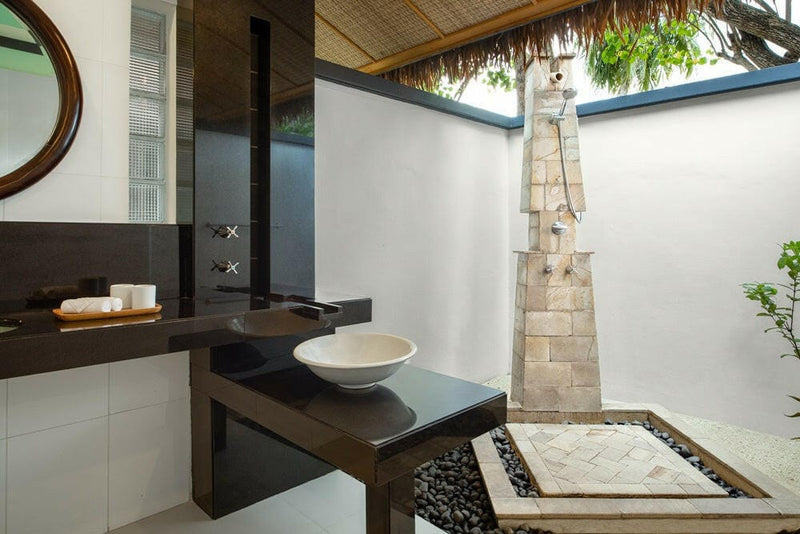 An outdoor shower at Dhawa Ihuru, stone clad column set in pebbles under a thatched roof.