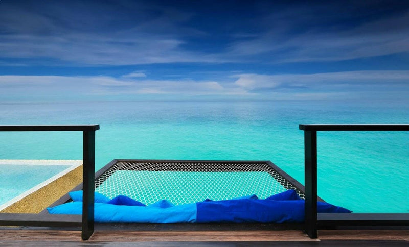 A blue deck daybed set over the water at Coco Bodu Hithi, the villa pool beside it and open ocean ahead