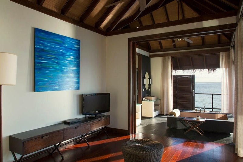 A villa living area at Coco Bodu Hithi, a blue canvas above the timber console and the deck through the doorway