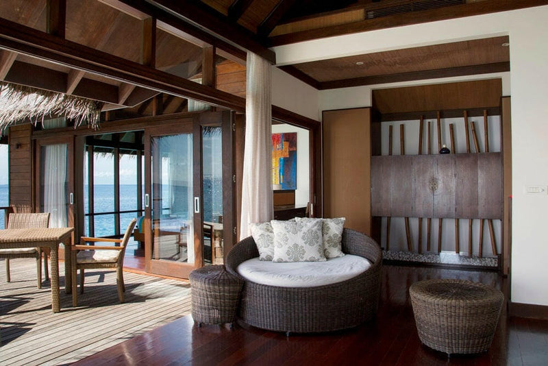 A round rattan daybed and two woven chairs in a villa at Coco Bodu Hithi, the deck and sea beyond