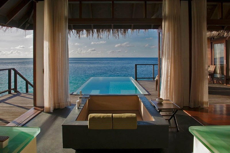 A villa infinity pool at Coco Bodu Hithi seen past the sofa and curtains, the ocean level with the water