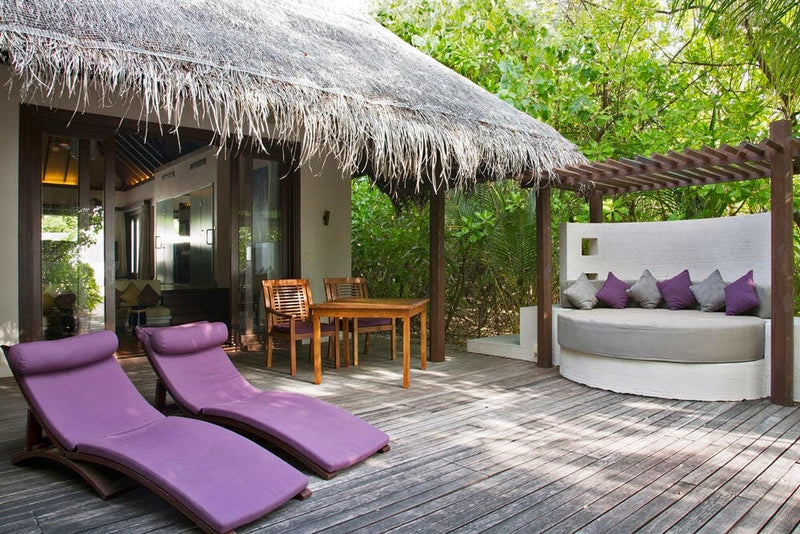 A villa deck at Coco Bodu Hithi, purple loungers and a round daybed beside a timber dining table