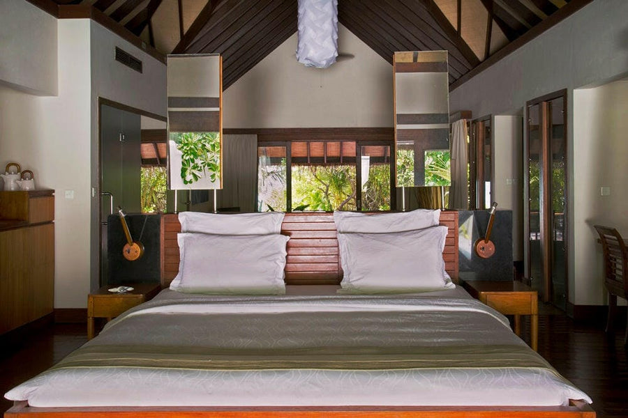 A villa bedroom at Coco Bodu Hithi, a king bed in white linen under a high timber-beamed ceiling