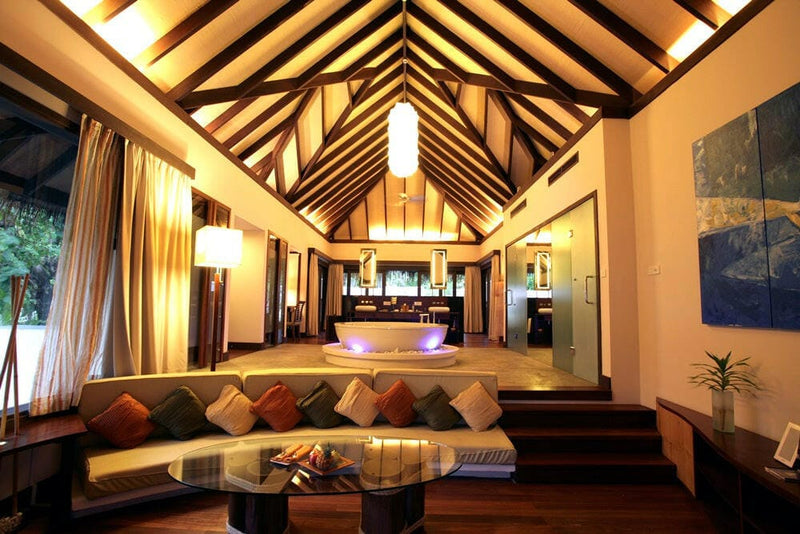 The living area of a villa at Coco Bodu Hithi, a low sofa with orange and green cushions facing the bed