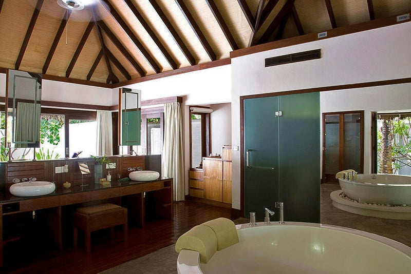 A villa bathroom at Coco Bodu Hithi, twin basins, a round tub and a glass shower facing the garden