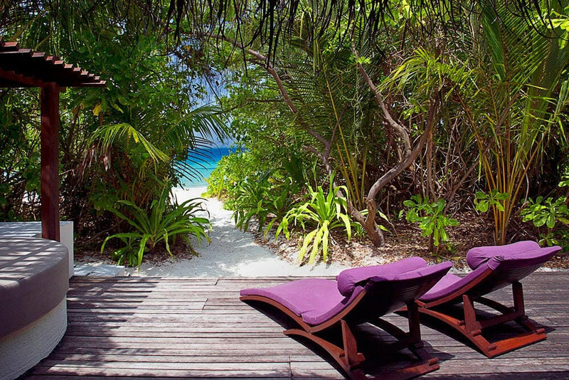 Two purple loungers on a villa deck at Coco Bodu Hithi, with a sandy path through the greenery to the sea