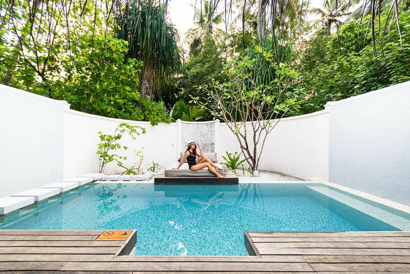 A guest sitting on the ledge of a walled garden pool at Coco Bodu Hithi, trees rising behind the wall