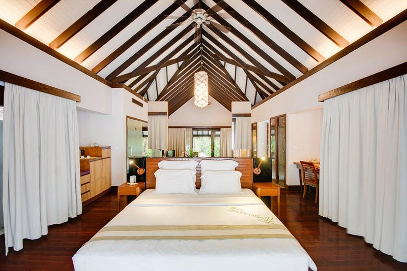 A villa bedroom at Coco Bodu Hithi, the bed framed by white curtains under a pitched beamed ceiling