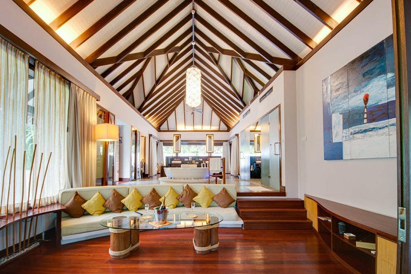 A villa sitting area at Coco Bodu Hithi, a long sofa in yellow cushions beneath a red abstract canvas