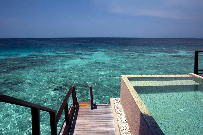 Deck steps down to the plunge pool of a water villa at Coco Bodu Hithi, reef water stretching beyond