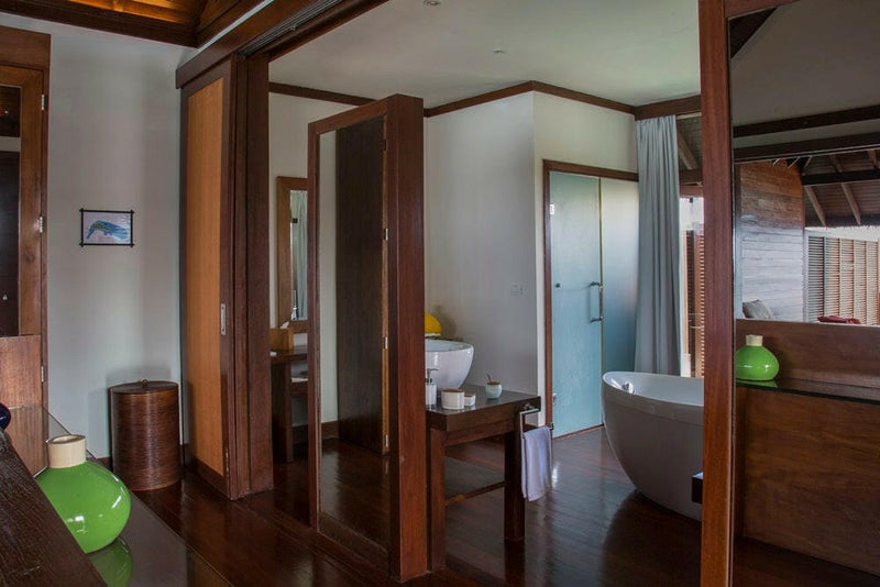 A villa bathroom at Coco Bodu Hithi, an oval freestanding tub seen through timber doorways