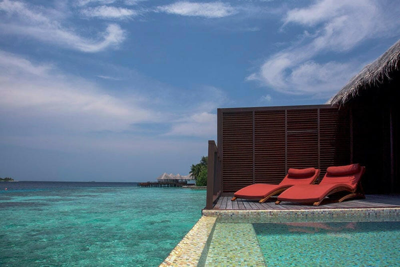 The deck of a water villa at Coco Bodu Hithi, two red loungers beside a plunge pool over the lagoon