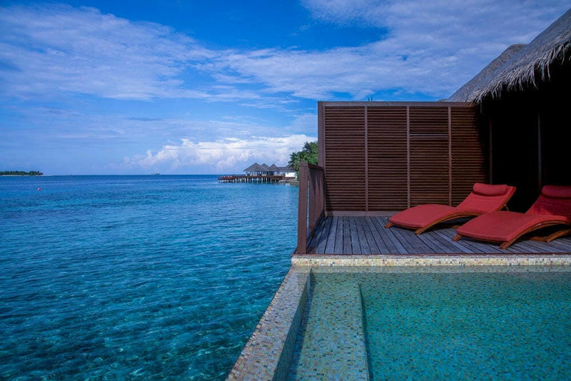 Red loungers and a plunge pool on a water villa deck at Coco Bodu Hithi, open ocean beyond