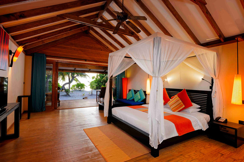 A beach villa bedroom at Canareef Resort Maldives, a four poster bed draped in white netting above an orange rug