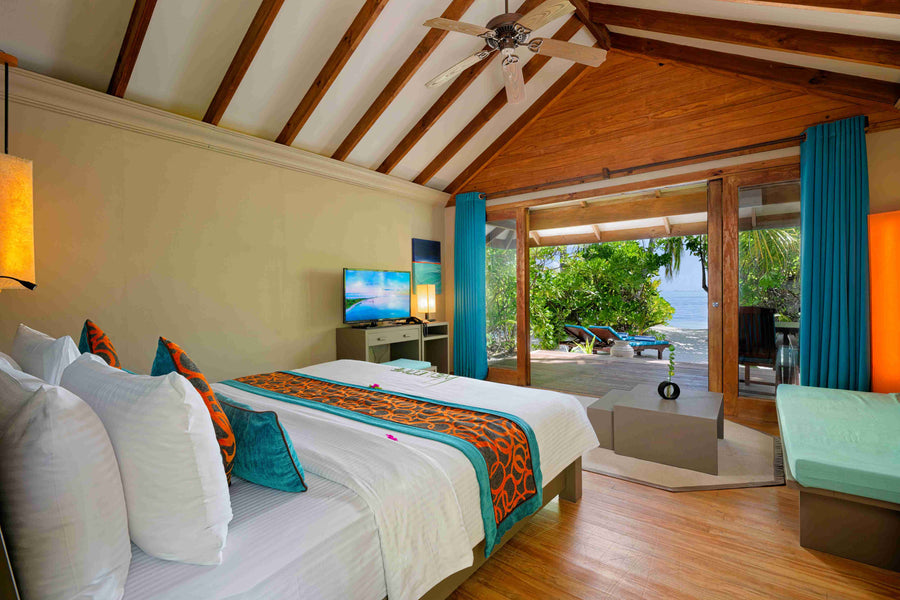 A beach villa bedroom at Canareef Resort Maldives, a patterned runner on the bed and a seating corner by the window