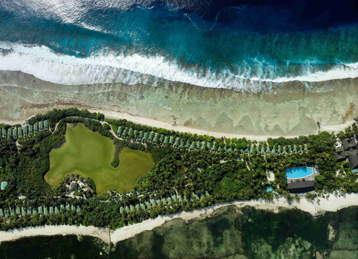 Canareef Resort Maldives from the air, the long wooded shoreline with surf breaking on the reef