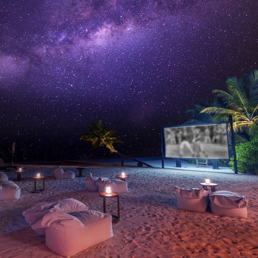 Beach cinema screen and loungers set up on the sand after dark