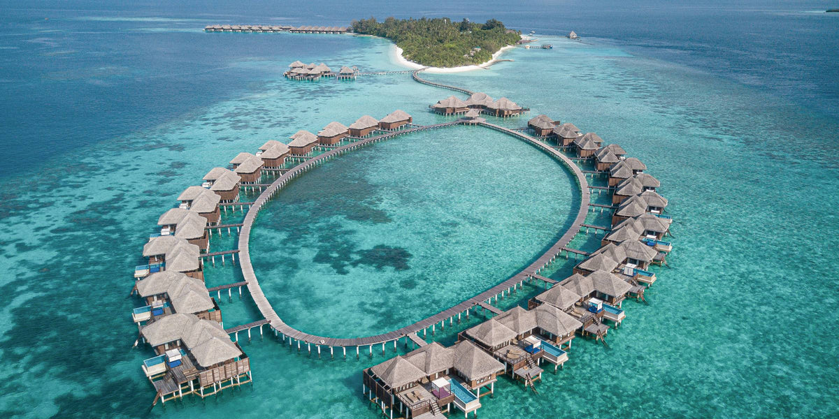 Coco Bodu Hithi Maldives from the air, a long loop of overwater villas across the lagoon