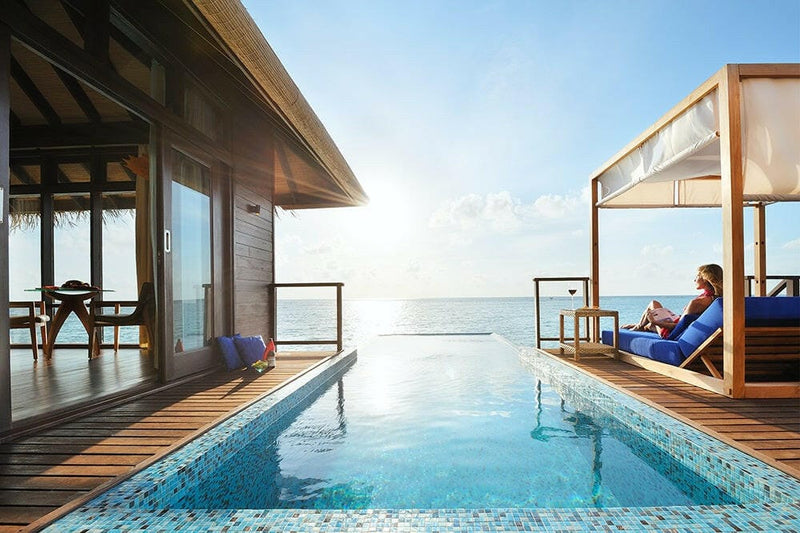 A guest on the canopied daybed at Coco Bodu Hithi, the villa's infinity pool running out to the sea