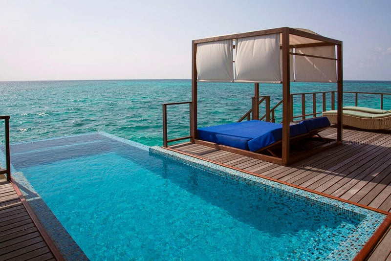 The timber deck of a villa at Coco Bodu Hithi, its infinity pool and canopied daybed above turquoise water